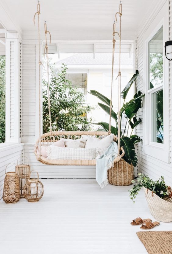 a heavenly white porch with a hanging bench, woven lanterns and baskets and a jute rug