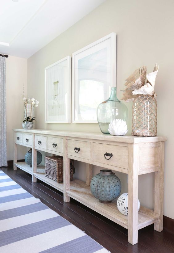 A long whitewashed console with sea inspired artworks, large bottles and lanterns and shells