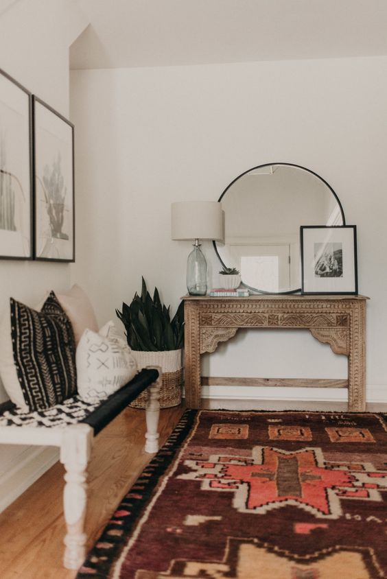 a boho entryway with a vintage encrusted console, a woven bench, pillows, artworks and succulents