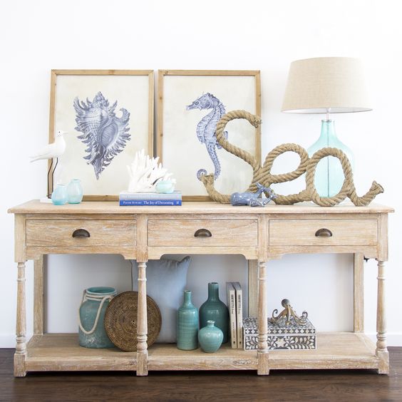 a light-colored wooden console, a rope artwork, painted bottles and a duo of sea creature artworks