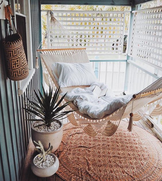 a small screened porch with a woven hammock, potted succulents and a boho printed rug