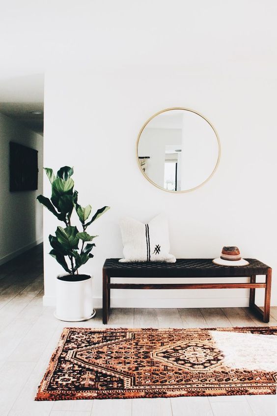 A boho rug, a woven leather bench, a faux fur pillow, a round mirror, a potted plant are an ideal combo