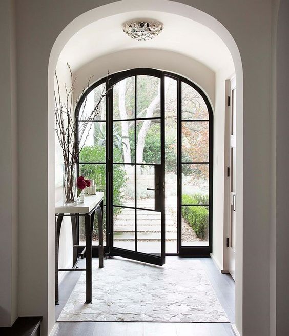 a fully glazed arched door with black metal framing is a chic and refined idea for any home