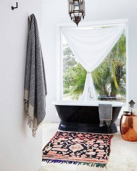 A serene boho chic bathroom with a boho rug, a free standing bathtub, a Moroccan lantern and a copper side table