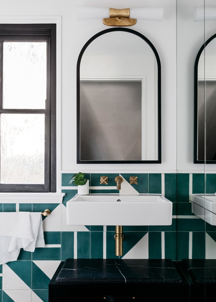 The bathroom is done with amazing green geometric tiles, black marble touches and brass fixtures