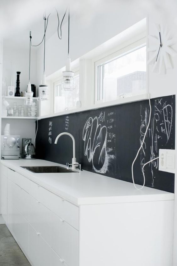 a minimalist white kitchen with a chalkboard backsplash that helps it stand out and look more interesting