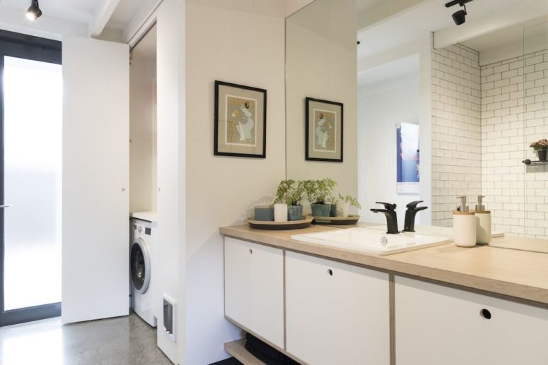 The bathroom features a hidden storage space and sleek modern furniture plus light-colored wooden touches