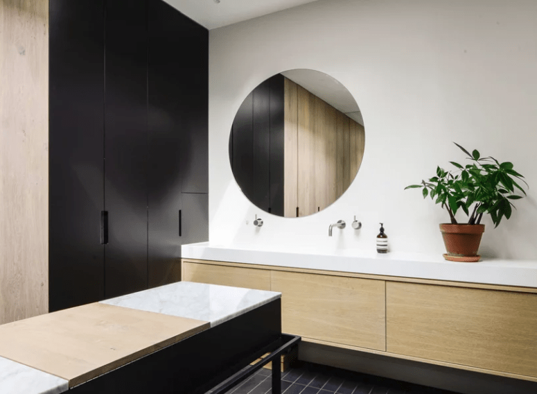 The bathroom is done in black and white with light-colored wood and marble for a chic look