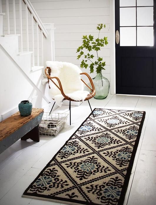 a rug, a wood and metal bench, a rattan chair with faux fur, a metal basket