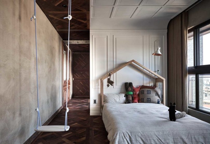 The kids' room is done with a swing, a house-shaped bed and concrete and molding walls