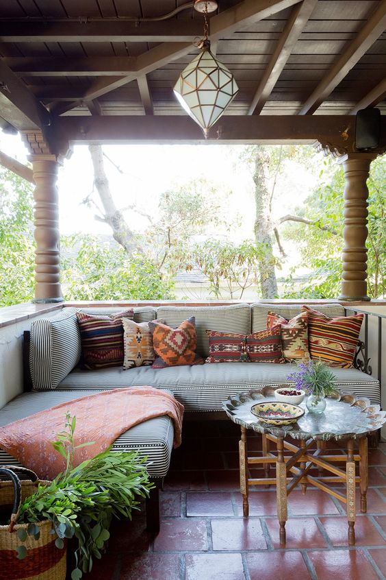 a screneed porch with a striped corner couch, a lantern, a side table and much greenery