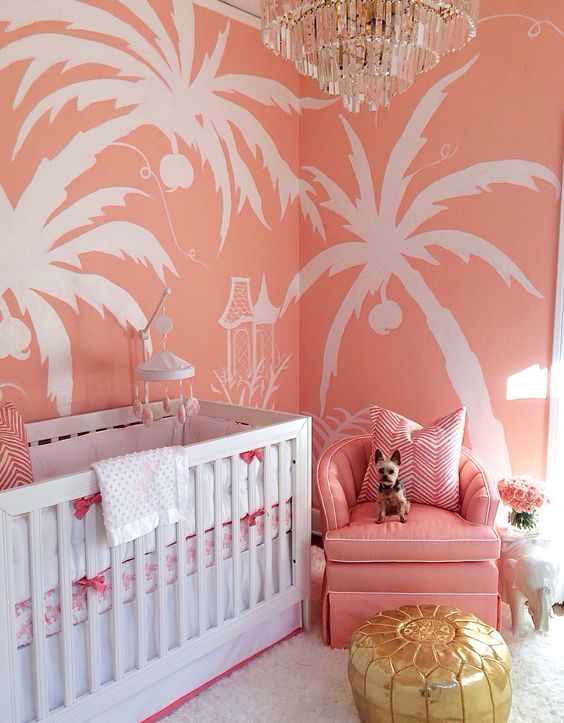 a colorful glam nursery with pink tropical print walls, a pink chair, a glam chandelier and a shiny ottoman