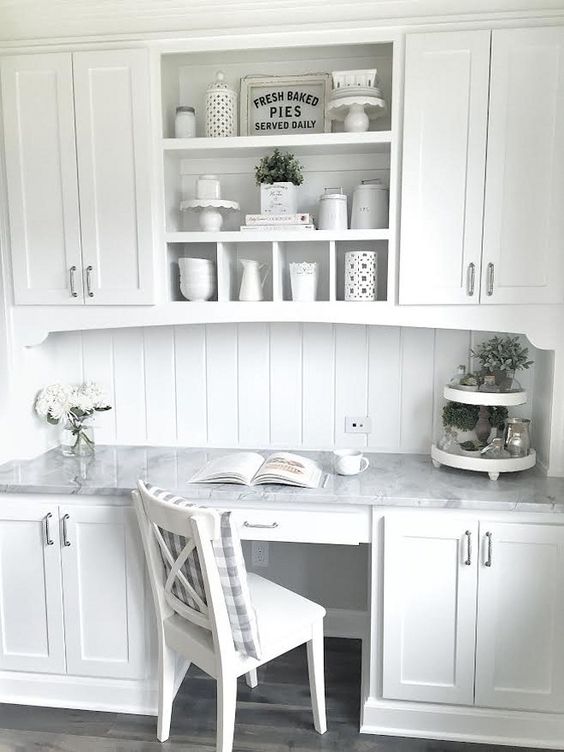 A vintage inspired white kitchen with a seamlessly built in desk with a marble countertops