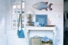 11 a whitewahsed entryway with a small table, a fish figurine, baskets, driftwood and corals for decor