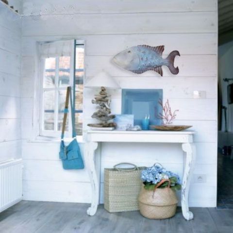 a whitewahsed entryway with a small table, a fish figurine, baskets, driftwood and corals for decor