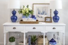 12 a white vintage console with bold blue lamps and vases, plants in pots, baskets and corals