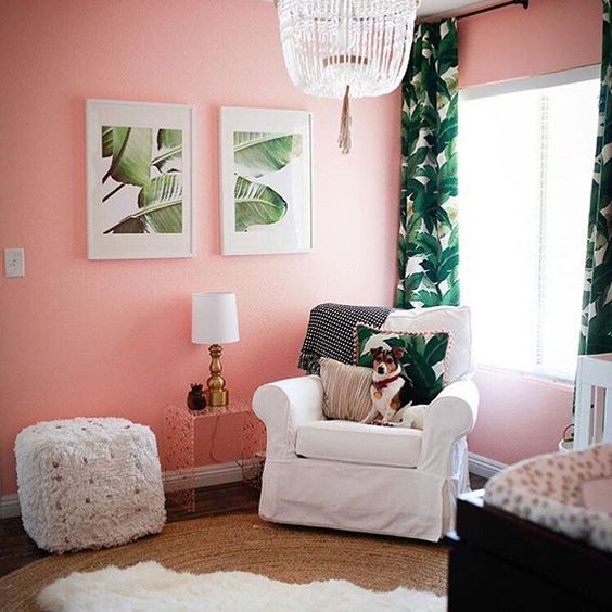 a girl's nursery with pink walls, a crystal chandelier, faux fur and tropical leaf artworks and textiles