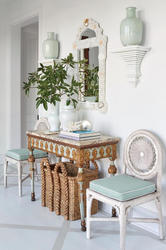 a whimsy and luxurious beach entryway with aqua touches, a basket for storage, white woven chairs, an encrysted console and a shell clad mirror