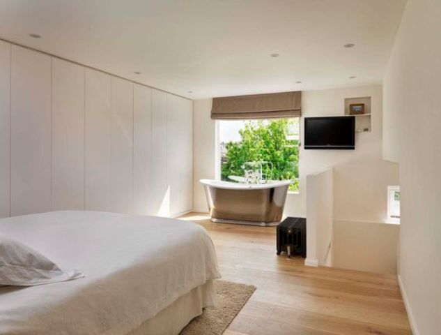 A contemporary bedroom with sleek storage cabinets and a metal free standing bathtub by the window