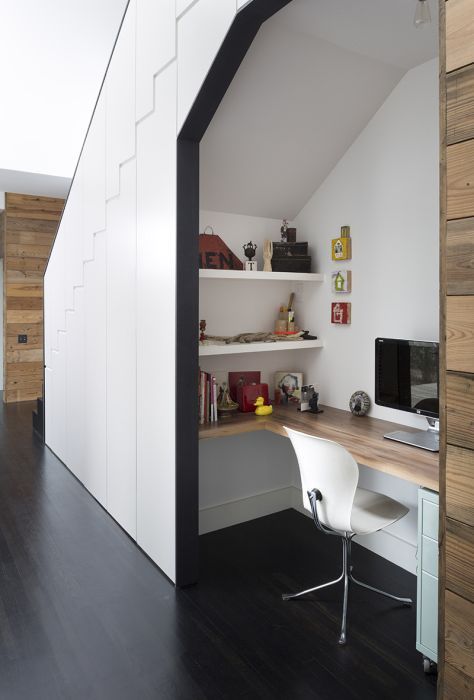 A contemporary home office space built inside a staircase with a built in desk, shelves and a chair