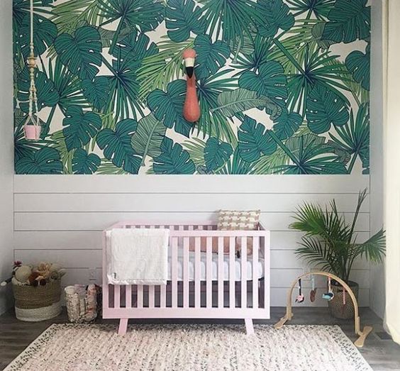 a simple tropical space with a palm leaf statement wall, a pink crib, a faux flamingo head on the wall