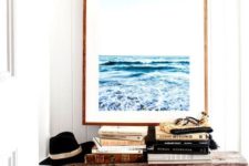 16 a beachy entryway with an oversized sea-inspired artwork, a wooden bench, a wooden bowl, books and a hat