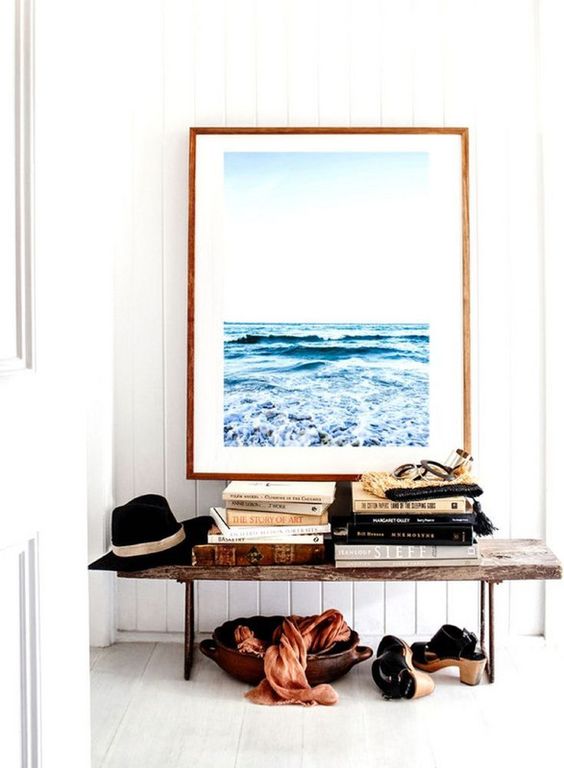 a beachy entryway with an oversized sea-inspired artwork, a wooden bench, a wooden bowl, books and a hat