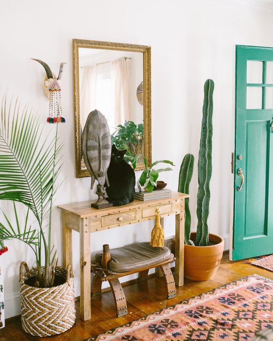 A boho rug, a console, a stool, a mirror, some plants and a cactus plus folk decor for a boho feel