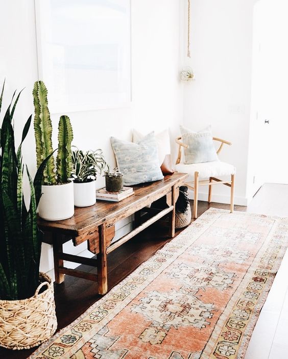 a boho rug, a vintage wooden bench, a chair, pillows and cacti and succulents in pots