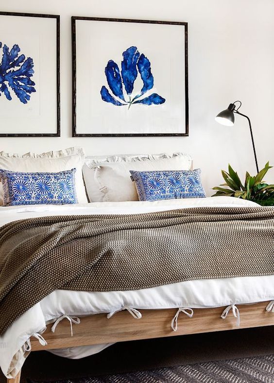 a textural bedspread, pritned pillows and bold blue artworks over the bed refresh the neutral space