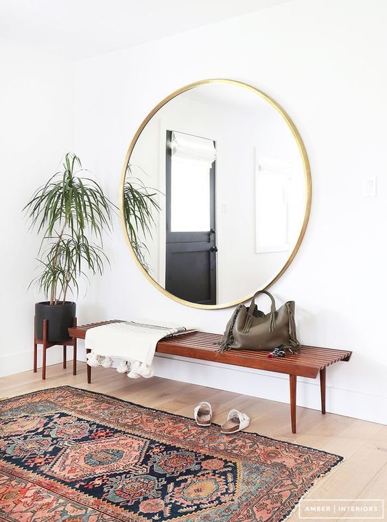 A boho rug, a wooden bench, an oversized round mirror, a potted plant