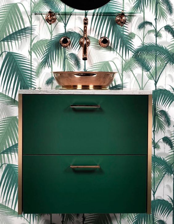 a chic dark green floatign vanity with copper touches and a palm leaf wall for en elegant look