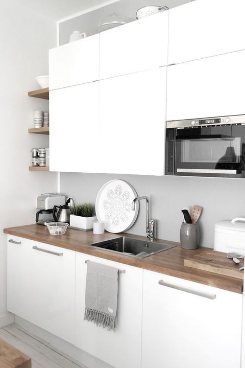 A minimalist white kitchen with a wooden countertop and a sleek concrete backsplash for an edgy feel