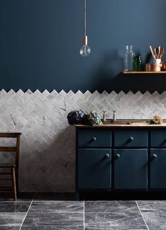 a navy kitchen with copper touches, wood and a grey marble chevron clad backsplash that adds interest