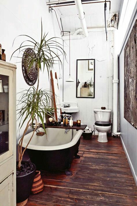 A boho bathroom with wooden floors, antique furniture, a free standing bathtub and potted greenery