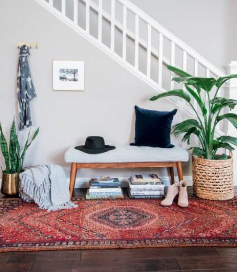 a boho rug, an upholstered bench, potted plants, some books under the bench