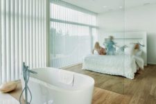 19 a minimalist bedroom and a bathtub separated with a glass divider so that both zones made a benefit from the views