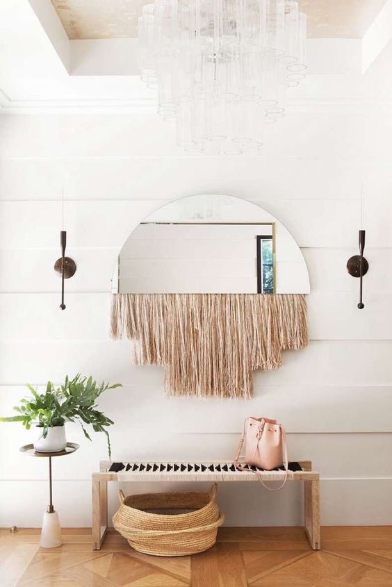 a boho space with a woven bench, a woven basket, a mirror with fringe and a potted plant