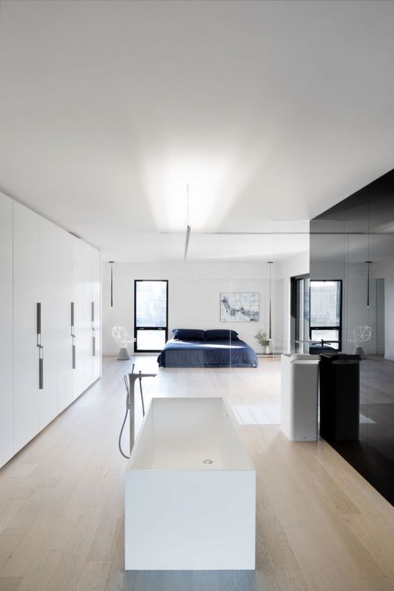 A minimalist spacious bedroom with a white free standing bathtub and a sink separated only with a glass space divider