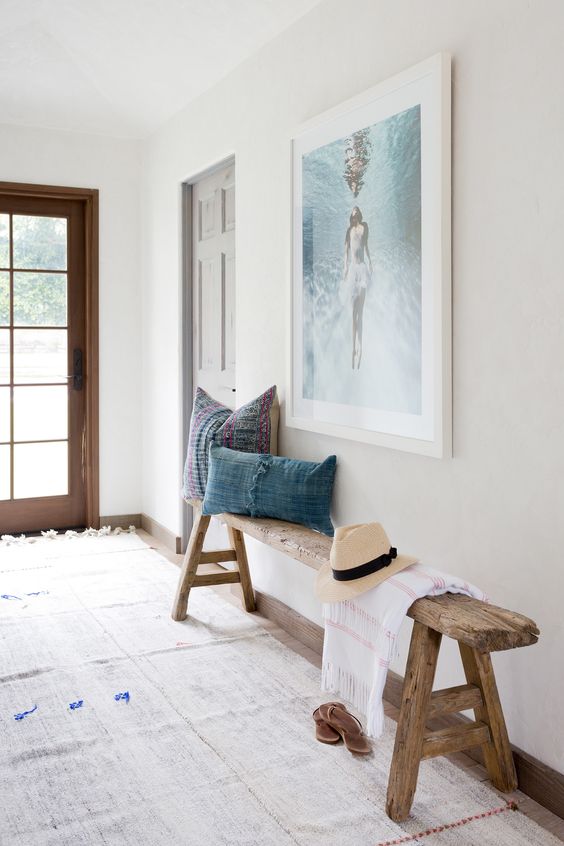 A reclaimed wood bench with trestle legs, chambray pillows, a sea inspired artwork over the bench