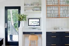 22 a stylish navy and white kitchen with a separated tiny office nook space with a built-in desk and shelves and a stool