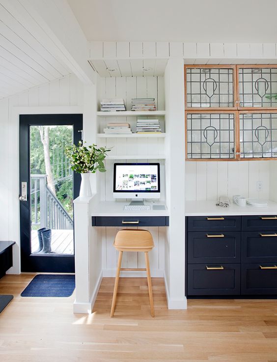 A stylish navy and white kitchen with a separated tiny office nook space with a built in desk and shelves and a stool