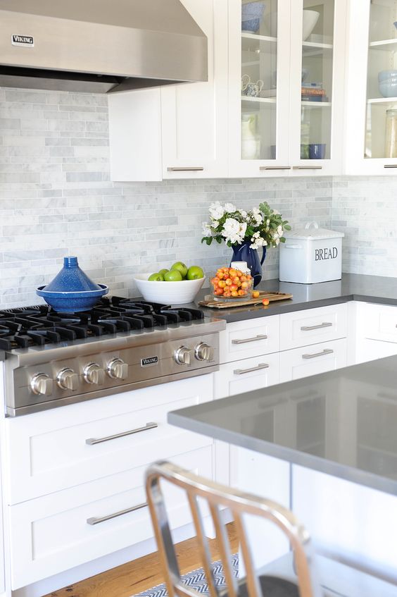 a white kitchen with grey countertops and a grey marble tile backsplash for a fresh modern look