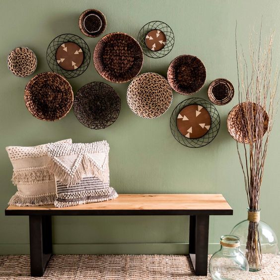 a wood and metal bench, woven and fringe pillows, an arrangement of plates and some branches