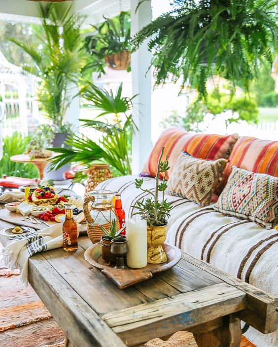 a super colorful boho porch with bold printed textiles, a pallet side table, greenery in pots and woven lanterns