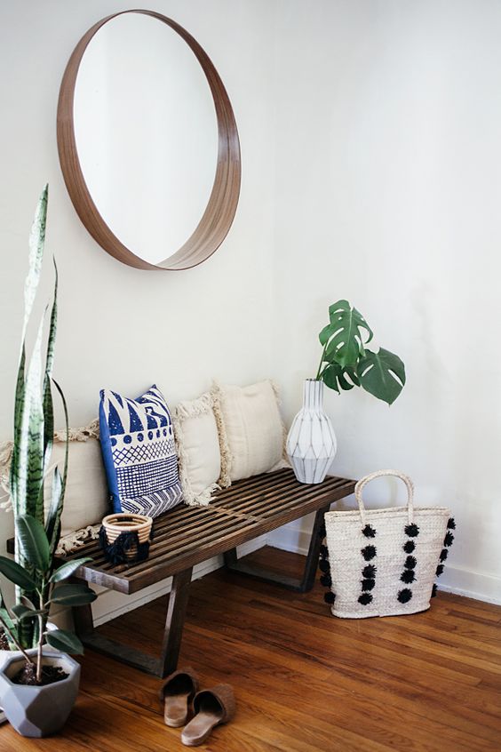 A wooden bench, a wood framed mirror, potted succulents and tropical leaves