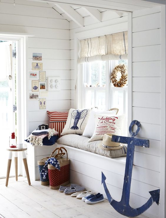 a whitewashed beach entryway with a windowsill bench, a stool, a shell wreath and some printed pillows