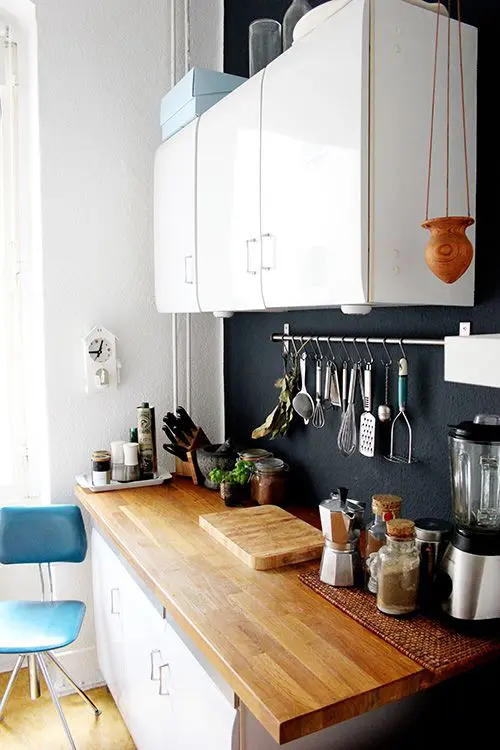 A cozy small white kitchen with a light colored countertop and a chalkboard backsplash that adds style