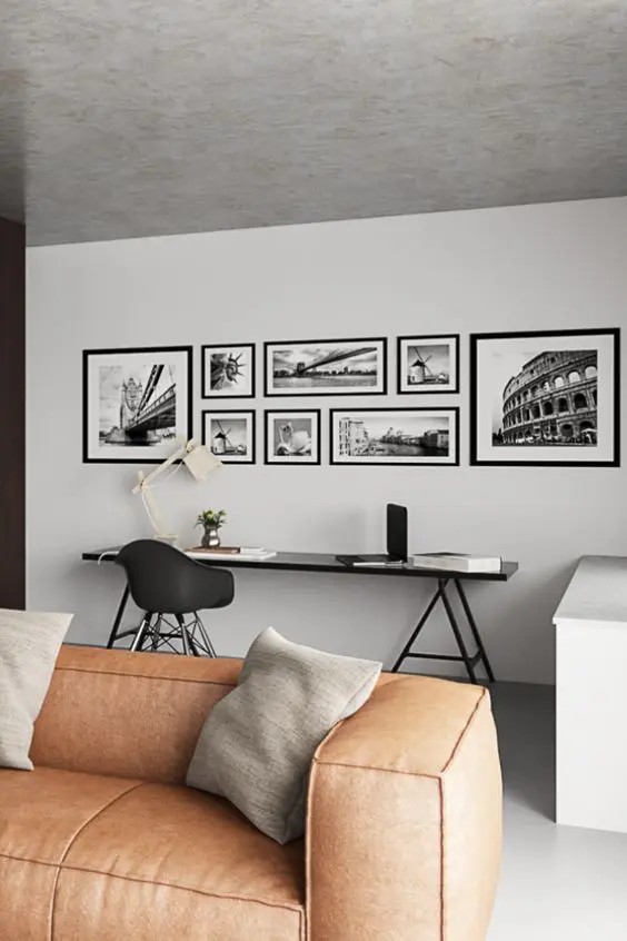 a Scandinavian living room with a black trestle desk, an amber leather low sofa, grey pillows, a gallery wall