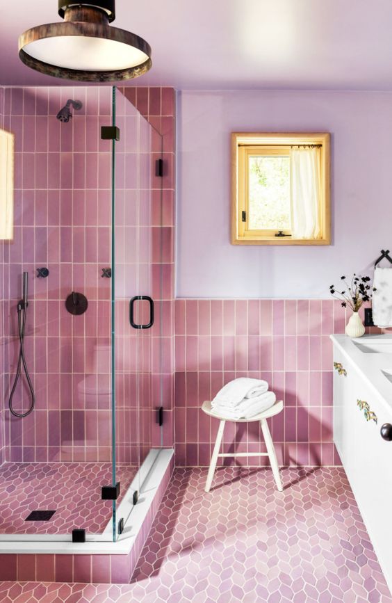 a bathroom with lilac walls and pink skinny and leaf-shaped tiles, a shower space, a white vanity and greenery is lovely